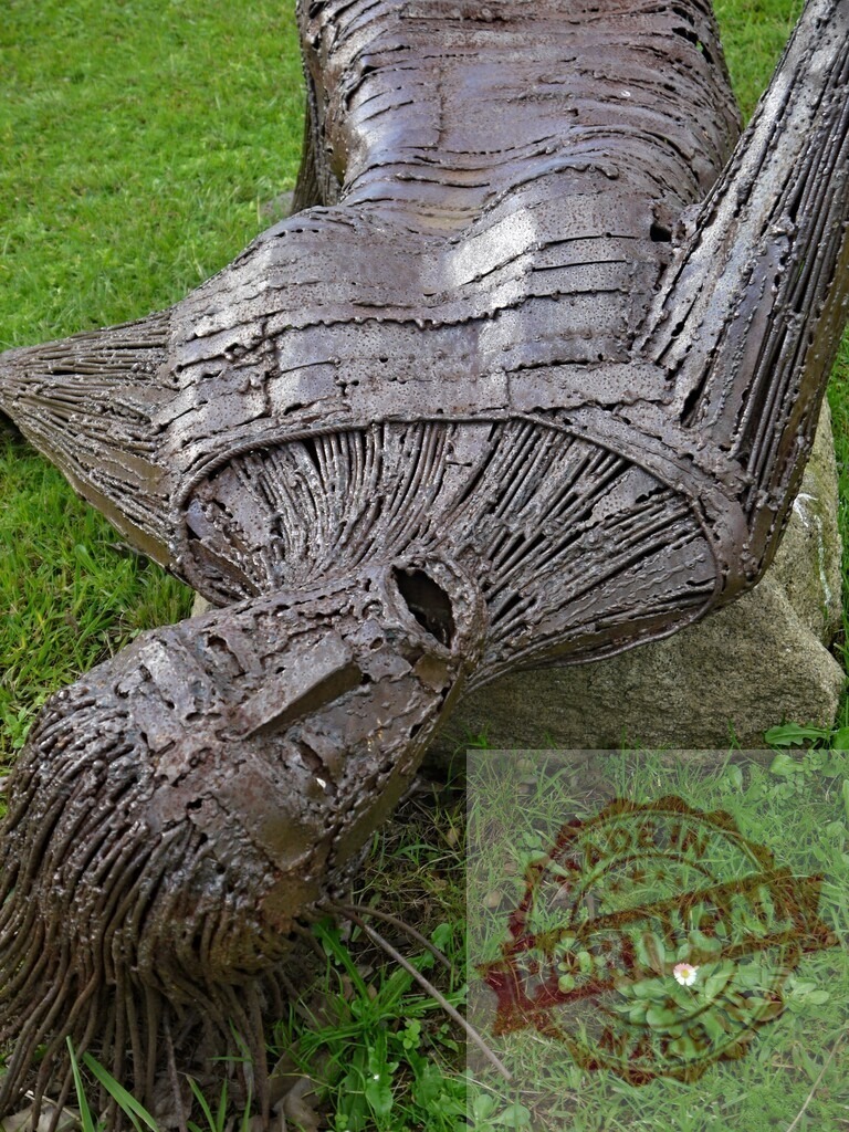 Abstract metal sculpture depicting human form on grass | Weathered iron abstract sculpture showcasing a reclining human figure in a green outdoor garden - Realisiert mit Pictrs.com