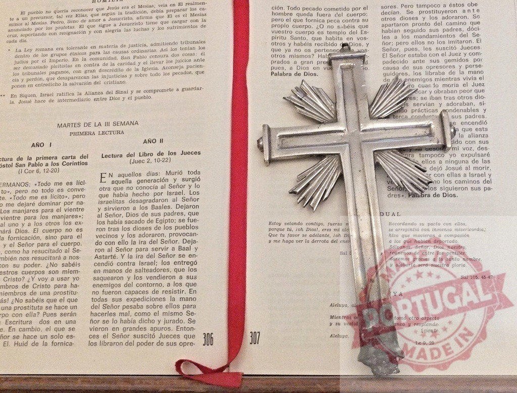 Silver crucifix lying on open Bible with red ribbon bookmark | Silver crucifix with stylized rays of light emanating from center, resting on open page of Spanish Bible with red ribbon bookmark - Realized with Pictrs.com