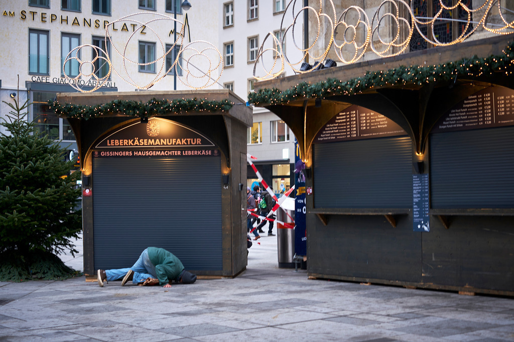 Mann sucht nach Essensreste am Weihnachtsmarkt | Wien, Austria - November 22, 2021: Massnahmen zur Einschränkung von COVID-19; Mann sucht nach Essensreste unter den Markständen am gesperrten Weihnachtsmarkt. - Realisiert mit Pictrs.com