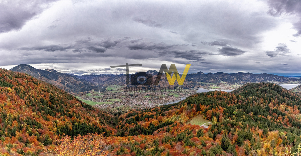 Herbst Panorama über das Tegernseer Land--Bunte Landschaft | Die Ansicht zeigt den Blick auf den Tegernsee und die umliegende Berglandschaft, in sehr schönen Herbstfarben.  Der Riederstein ist ein 1207 m hoher Felssporn in den Bayerischen Voralpen, etwa 481 Höhenmeter über dem Tegernsee gelegen. Die neugotische Riedersteinkapelle befindet sich auf diesem Felssporn. Das Bild zeigt die Region in herbstlichen Farben mit bewaldeten Hängen und einem Talbereich mit Siedlungen. - Realisiert mit Pictrs.com