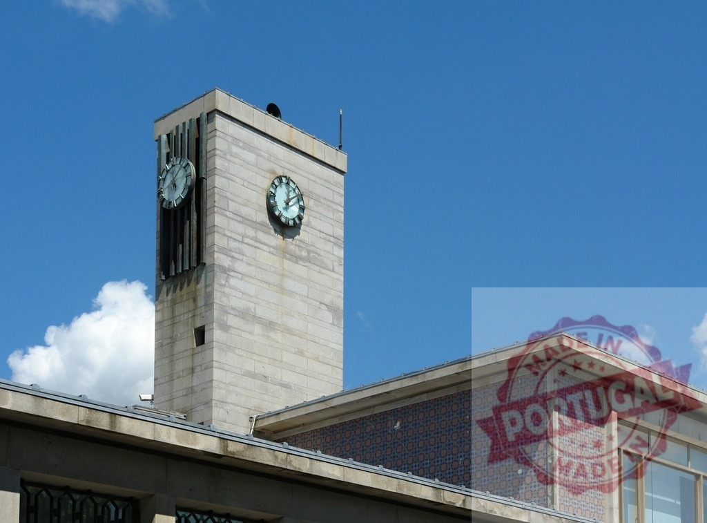 Clock tower indicating time on modern building facade. Portugal - Norte | Modern clock tower standing against a clear blue sky, featuring ceramic tile mosaic - Realized with Pictrs.com