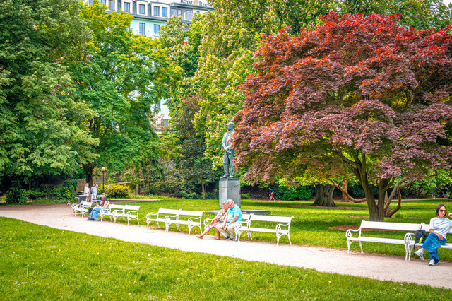 Besucher entspannen im Stadtpark in Karlsbad. Bänke stehen entlang des Weges. | Besucher entspannen im Stadtpark in Karlsbad. Bänke stehen entlang des Weges. - Realisiert mit Pictrs.com