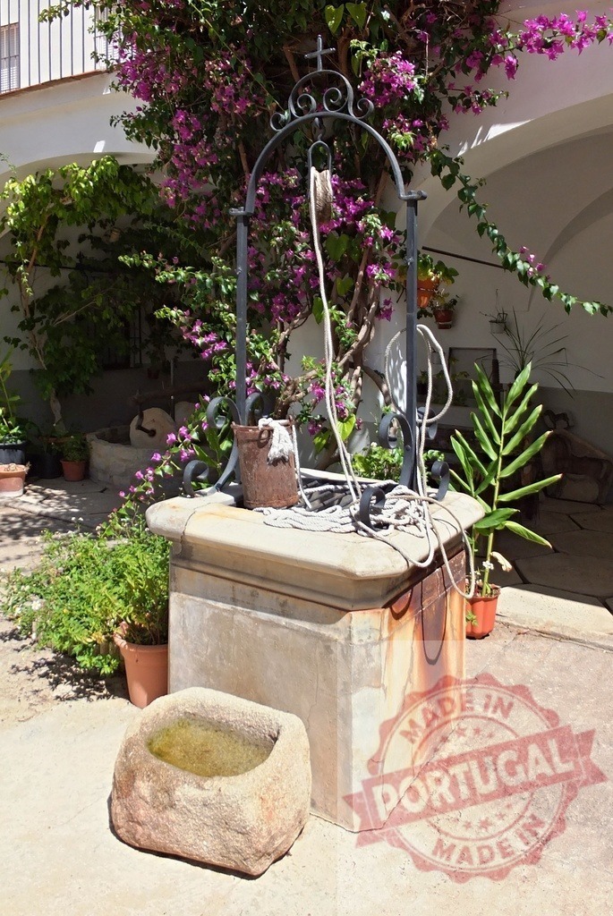 Traditional stone well in a sunny Mediterranean courtyard | Old stone well with a metal arch and rope bucket in a sunny Spanish courtyard - Realisiert mit Pictrs.com