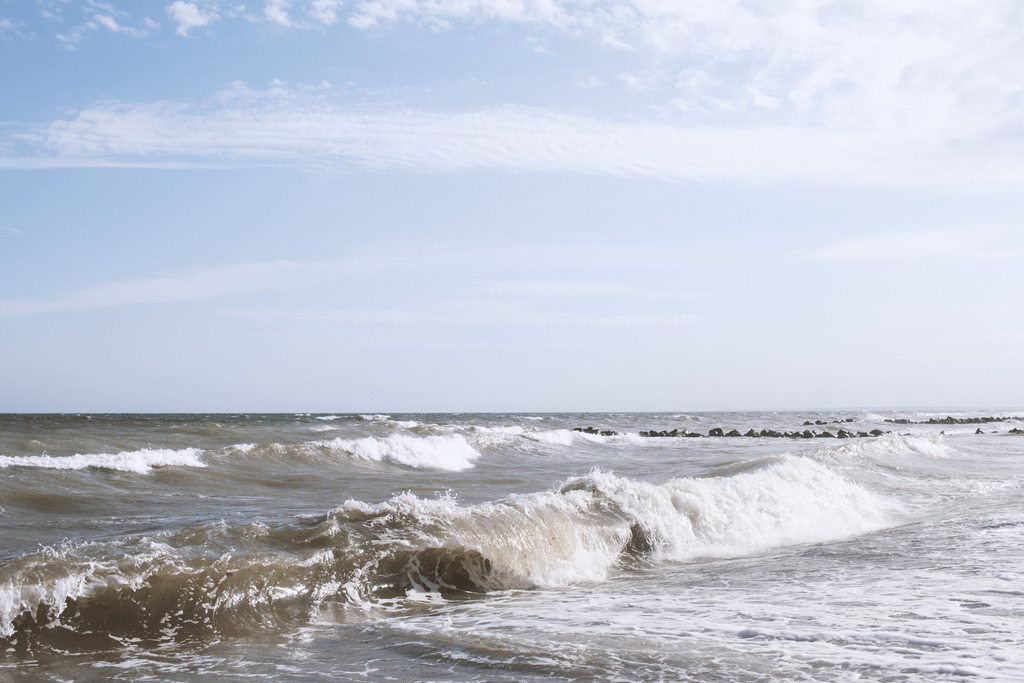 Wandbild: Schönhagener Brandungsmoment | Die Brandung in Schönhagen trifft mit kräftigen Wellen auf die Küste, weißer Schaum bricht über dem bewegten Wasser, und im Hintergrund liegt die Steinmole ruhig in der Ostsee. Der Himmel mit seinen hellen Wolken öffnet die Szene nach oben und verstärkt die Weite des Moments. Dieses Wandbild fängt die lebendige Kraft der Schönhagener Küste ein und bringt die frische, maritime Atmosphäre der Ostsee direkt in den Raum.