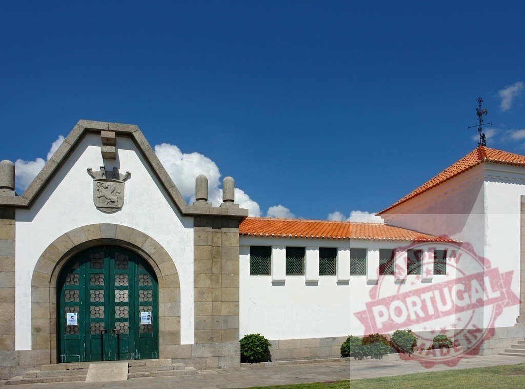Old Quinta da Bacalhôa building entrance with coat of arms. Region Norte - Portugal | Old building facade with arched entrance, stone details, and orange tile roof under blue sky - Realisiert mit Pictrs.com