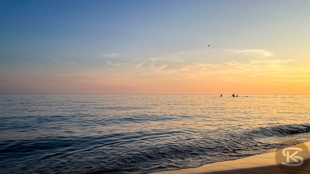 Sonnenuntergang am Mittelmeerstrand in der Camargue – Südfrankreich | Stimmungsvolles Panorama der Küste bei Saintes-Maries-de-la-Mer in der Camargue mit Sandstrand, ruhigen Wellen im goldenen Abendlicht und Silhouetten von Menschen im Wasser. - Realisiert mit Pictrs.com