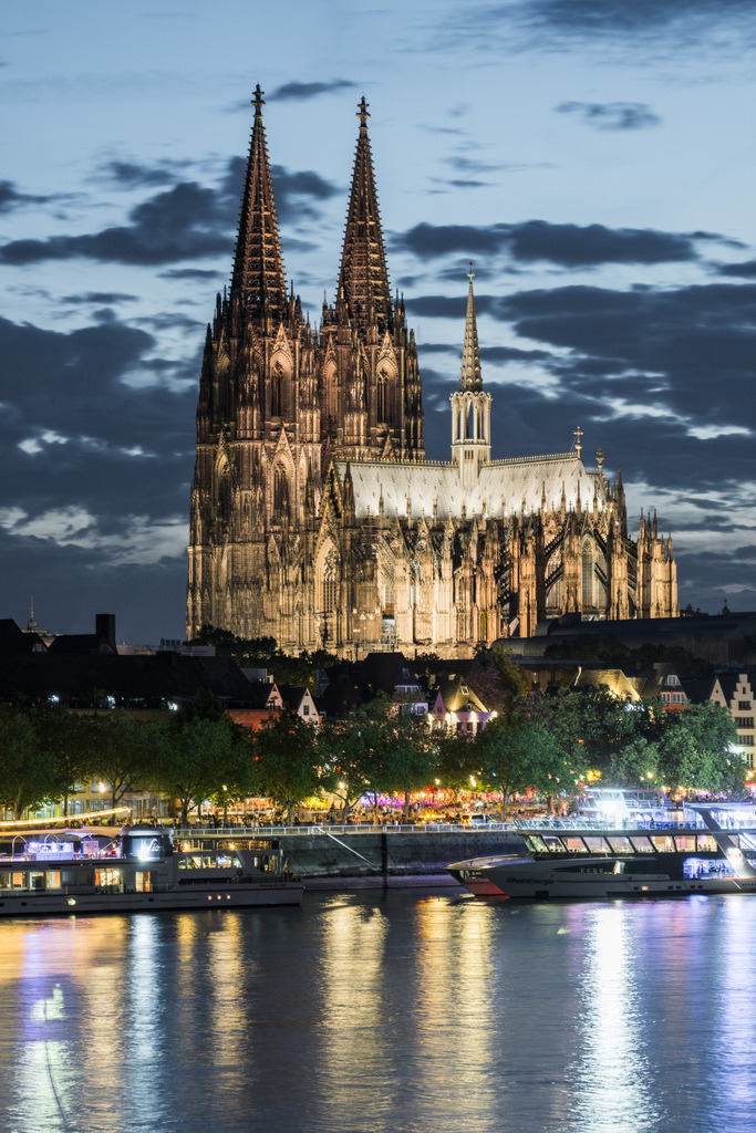 Kölner Dom am Rhein bei Nacht | Der beleuchtete Kölner Dom erhebt sich eindrucksvoll über dem Rhein. Die warme Architekturbeleuchtung spiegelt sich im Wasser und hebt die gotischen Türme vor dem dunklen Abendhimmel hervor. - Realisiert mit Pictrs.com