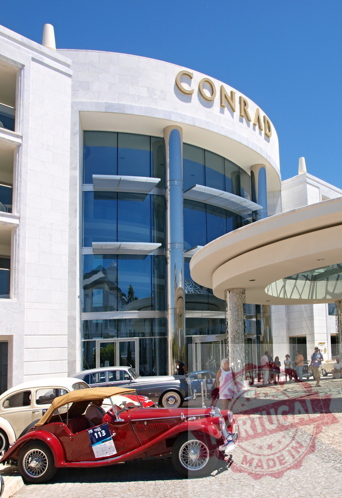 Red vintage car parked in front of Conrad Algarve Hotel | Shiny red vintage car parked outside the main entrance of Conrad Algarve Hotel, with tourists arriving - Realized with Pictrs.com