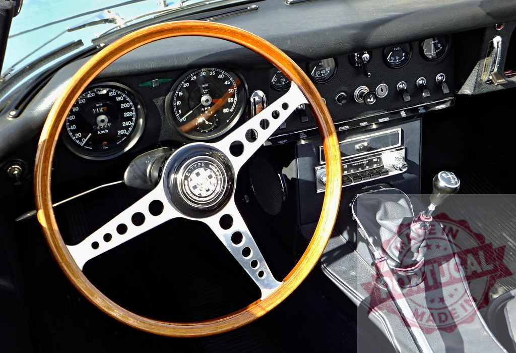 Wooden steering wheel and dashboard of a classic Jaguar E-Type sports car | Interior view of a vintage Jaguar E-Type, focusing on the wooden steering wheel, dashboard, and gear stick - Realisiert mit Pictrs.com