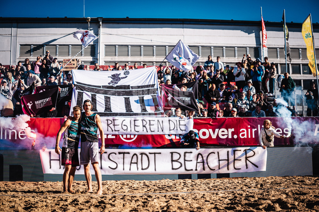 Beachvolleyball | Männer | Allianz German Beach Tour 2025 | Tourstop Berlin | 23.08.2025 | Einlauf von v.l. Eric Stadie-Seeber und Jannik Kühlborn, im Hintergrund die Fangruppe Fraktion Bräune mit einer Choreo und Pyrotechnik, Hier Regieren Die Hauptstadt Beacher