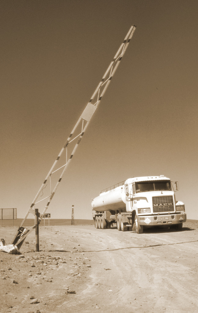 Starker Truck vor fragiler Schranke | Sepiafotografie eines Tanklastwagens vor einer Schranke in karger Landschaft – Sinnbild für Macht, Begrenzung und das Innehalten vor Grenzen. - Realisiert mit Pictrs.com