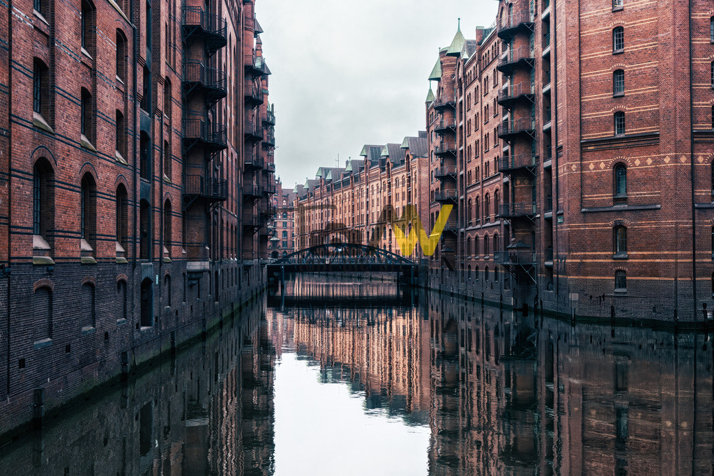 Einblick in die Speicherstadt mit den gespiegelten Backsteingebäuden,Hamburg | Das Bild zeigt die Speicherstadt in Hamburg, ein historisches Lagerhausviertel und UNESCO-Weltkulturerbe. Die Speicherstadt wurde von 1885 bis 1927 erbaut und liegt südlich der Hamburger Altstadt zwischen Oberhafen und Sandtorkai. Sie ist bekannt für ihre charakteristischen Backsteingebäude und Fleete (Kanäle). Zusammen mit dem Kontorhausviertel bildet sie das UNESCO-Weltkulturerbe „Speicherstadt und Kontorhausviertel mit dem Chilehaus“.  - Realisiert mit Pictrs.com