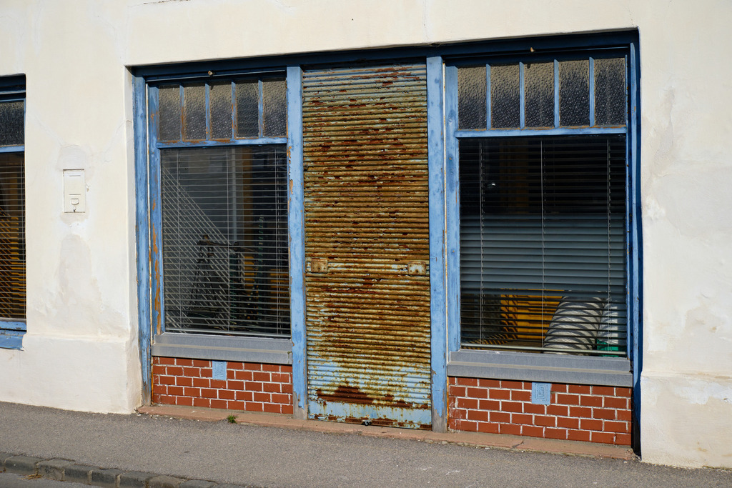 geschlossenes leeres Geschäft | Siebenhirten, Austria - March 09, 2025: geschlossenes leeres Geschäft mit rostigem Rollbalken. - Realisiert mit Pictrs.com
