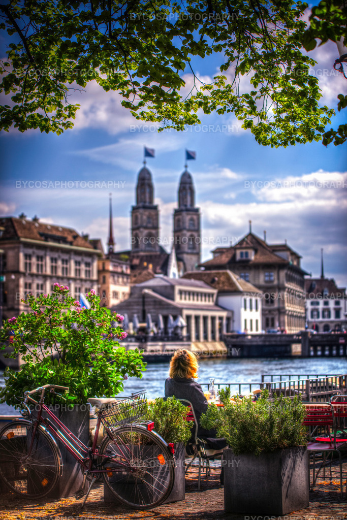 Zürich Spring Moments | Das ist nicht einfach nur Zürich – das ist das Lebensgefühl in Zürich. Kaffee, Fahrrad, Frühling, Blumen, Wasser, das Grossmünster im Hintergrund und eine Frau, die den Moment genießt. Das ist Lifestyle-Kunst, ein romantischer Stadtmoment, eine Postkarte der Stadt, aber auf höchstem künstlerischem Niveau.Eine warme und poetische FineArt-Fotografie fängt einen friedlichen Frühlingsnachmittag in Zürich ein.Unter dem sanften Grün der frisch erblühten Blätter sitzt eine Frau an der Limmat und genießt die Sonne und den zeitlosen Blick auf das Grossmünster. Fahrräder, Blumen und Cafés am Ufer verleihen dem Bild eine intime, authentische Atmosphäre des Stadtlebens.Dieser Druck bringt Wärme, Nostalgie und Charme in jeden Raum – perfekt für alle, die Zürich, Reisen und romantische Stadtmotive lieben. - Realisiert mit Pictrs.com