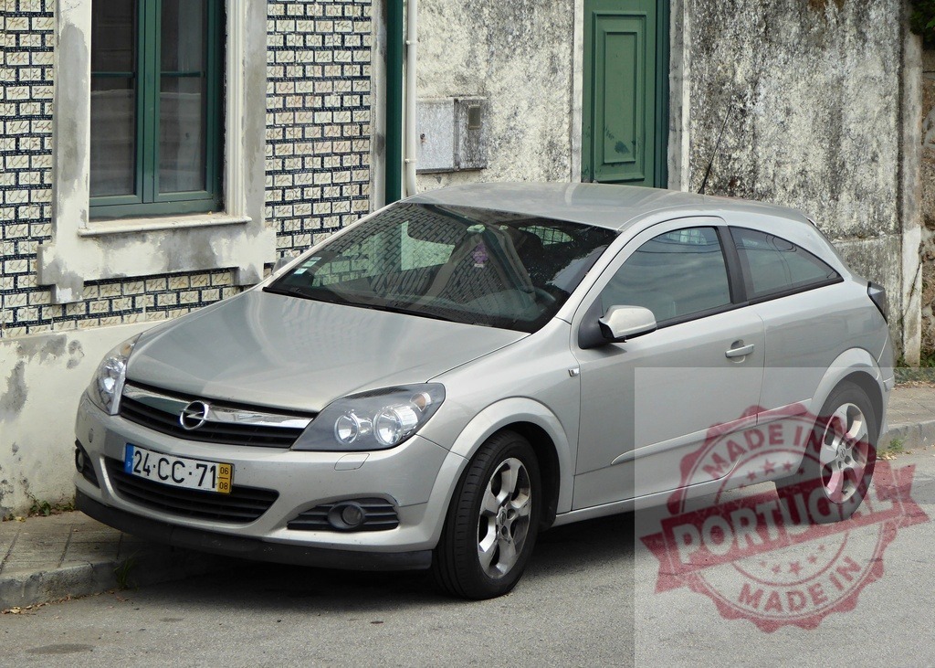 Silver Opel Astra hatchback parked on street | Silver Opel Astra hatchback car parked on a European street next to a building - Realized with Pictrs.com