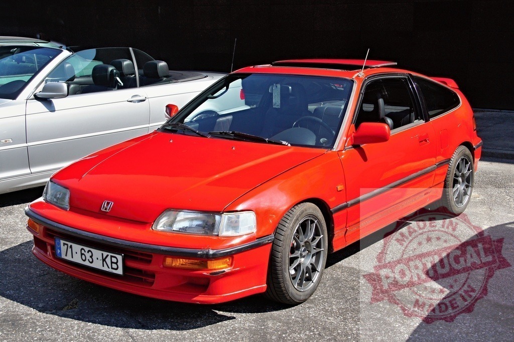 Red Honda CRX parked near a white convertible car | Shiny red Honda CRX parked outdoors, a white convertible car is visible in the background - Realized with Pictrs.com