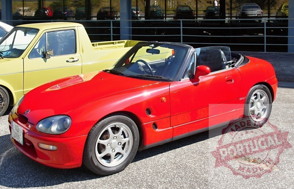 Red Suzuki Cappuccino parked near a yellow Volkswagen Caddy pickup truck | Shiny red Suzuki Cappuccino roadster parked in front of a yellow Volkswagen Caddy pickup truck in a parking lot - Realisiert mit Pictrs.com