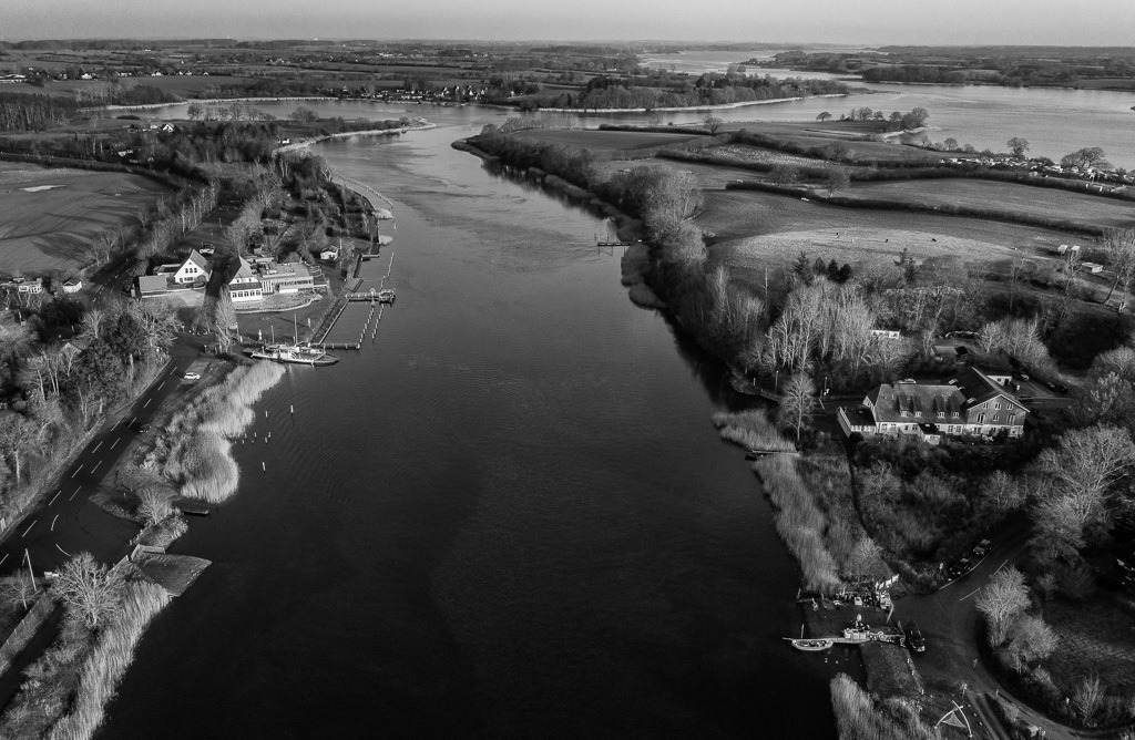 fischer-2019-520 | Blick auf die Schlei bei Missunde. Unten rechts ist die Ersatzübergangsstelle ("NATO-Rampe") zu sehen. Diesen Platz nutzt der Schleifischer Matthias Nanz als Anleger für seine Boote und als Lager. Hier ist er an einem sonnigen Tag im Dezember gerade von einer Fangfahrt auf Heringe zurückgekehrt. - Realisiert mit Pictrs.com