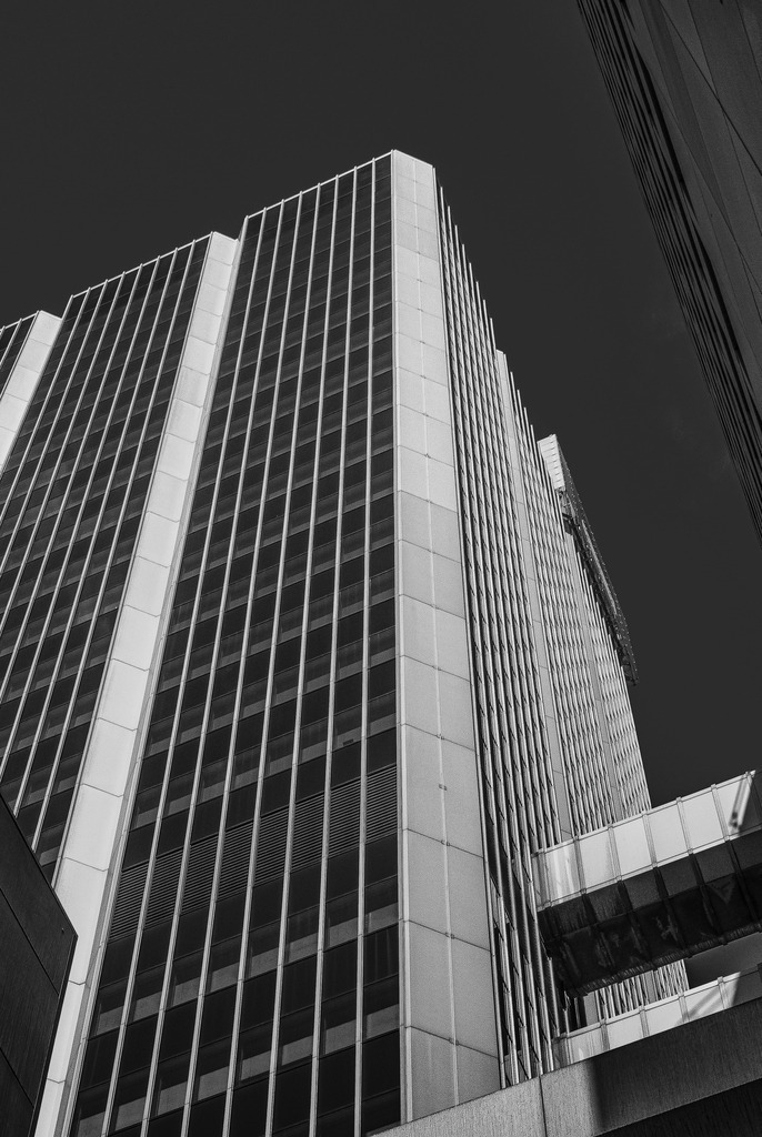 Vertical Precision | Ein reduziertes Schwarz-Weiß-Foto moderner Architektur in Düsseldorf. Die markante Hochhausfassade mit ihren klaren vertikalen Linien, starken Kontrasten und geometrischen Strukturen verleiht dem Motiv eine kraftvolle, zeitlose Wirkung. Die Perspektive von unten verstärkt die Präsenz des Gebäudes und lenkt den Blick in die Höhe. Ein minimalistisches Fine-Art-Motiv für Liebhaber urbaner Architektur, klarer Formen und moderner Bildsprache. - Realisiert mit Pictrs.com
