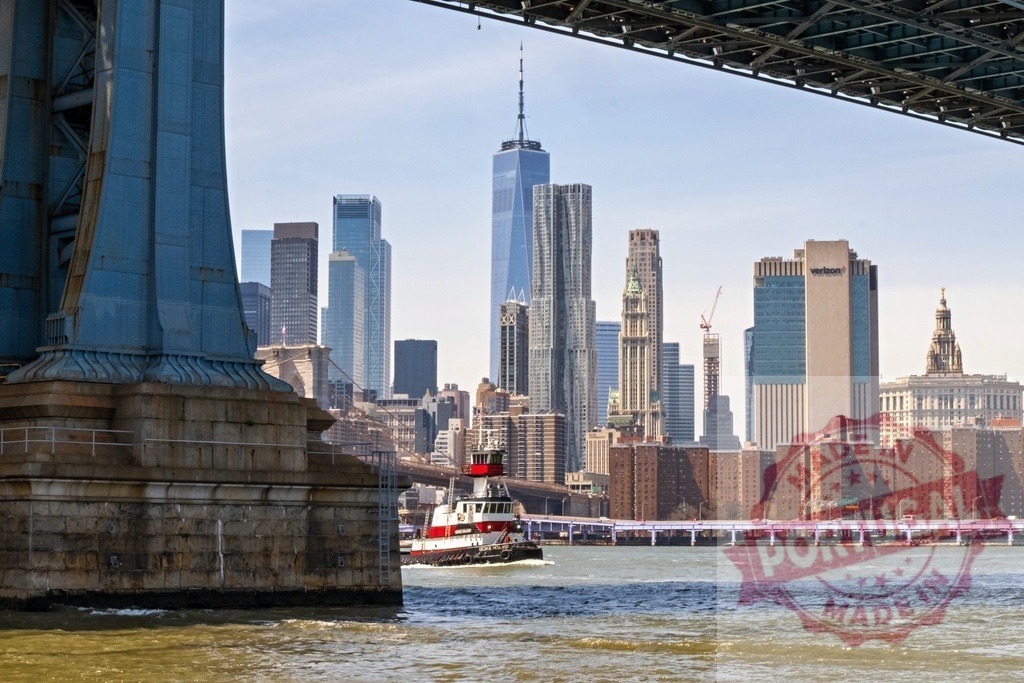 Tugboat sailing on East River with Manhattan skyline and Brooklyn Bridge in New York City | Red and white tugboat sailing on East River with One World Trade Center and Manhattan skyline in background, seen from under Brooklyn Bridge in New York City - Realized with Pictrs.com