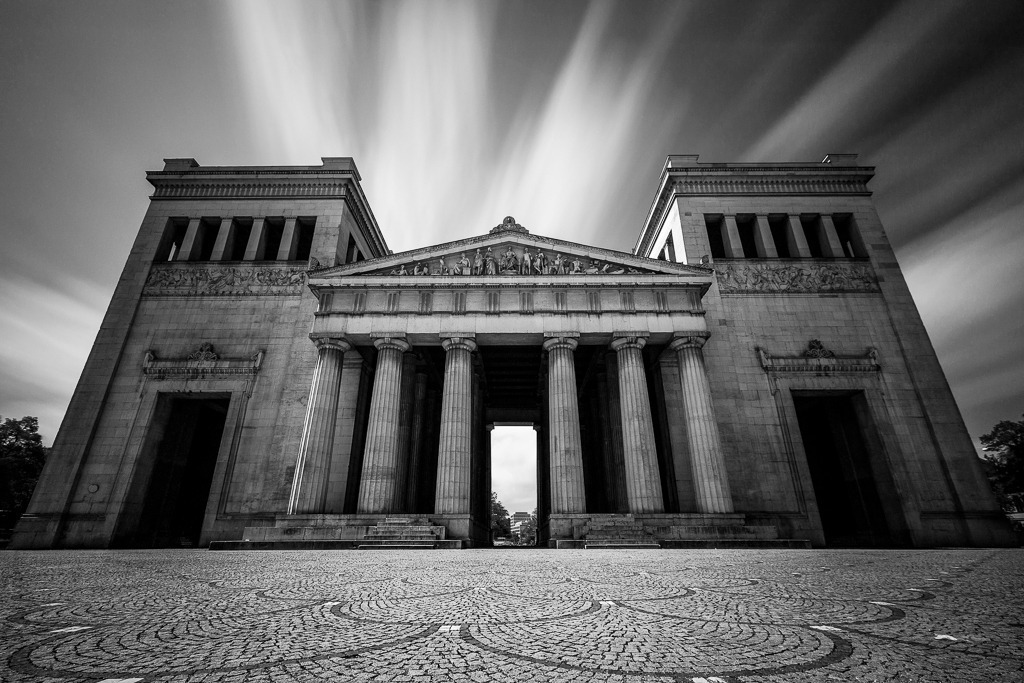 Zeitfluss – Langzeitbelichtung am Königsplatz | Die klassizistische Architektur des Münchner Königsplatzes trifft auf die Dynamik ziehender Wolken – festgehalten in einer Langzeitbelichtung. Das Zusammenspiel von starrer Monumentalität und fließender Bewegung erzeugt eine zeitlose Stimmung, die Vergänglichkeit und Beständigkeit in einem Bild vereint. Ein moderner Blick auf ein historisches Wahrzeichen. - Realisiert mit Pictrs.com