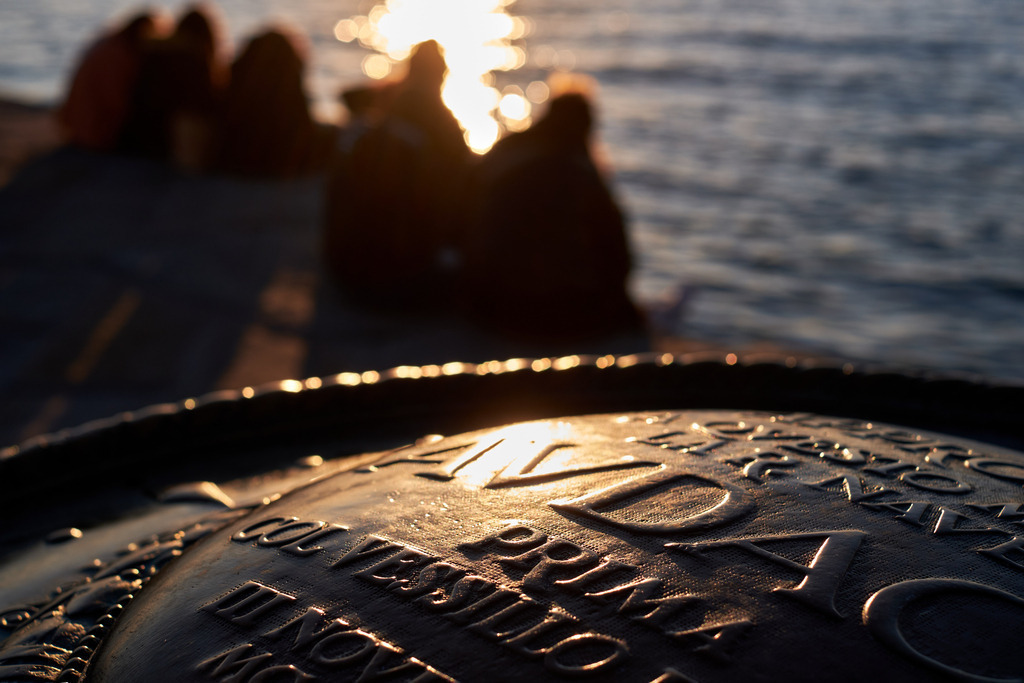 Junge Menschen sitzen an der Molo Audace im Sonnenuntergang | Triest, Austria - March 10, 2022: Junge Menschen sitzen an der Molo Audace im Sonnenuntergang. - Realisiert mit Pictrs.com