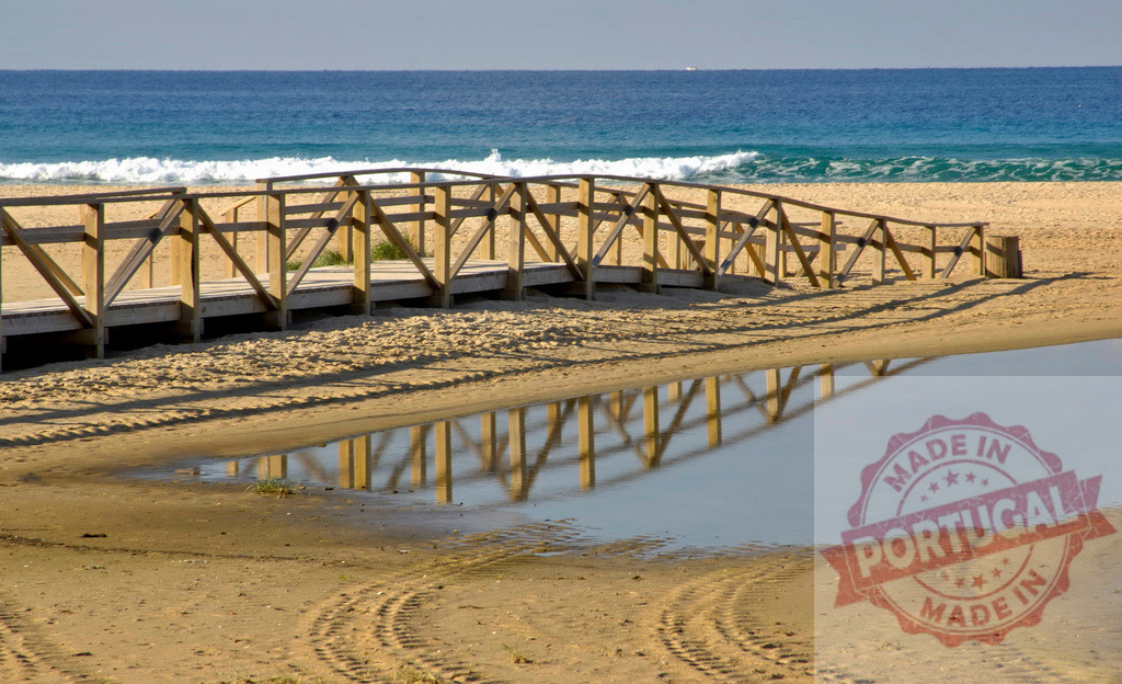 Wooden boardwalk reflecting in water on sandy beach. Espana - Cadiz | Wooden boardwalk reflecting in a pool of water on a sandy beach with the ocean beyond - Realized with Pictrs.com