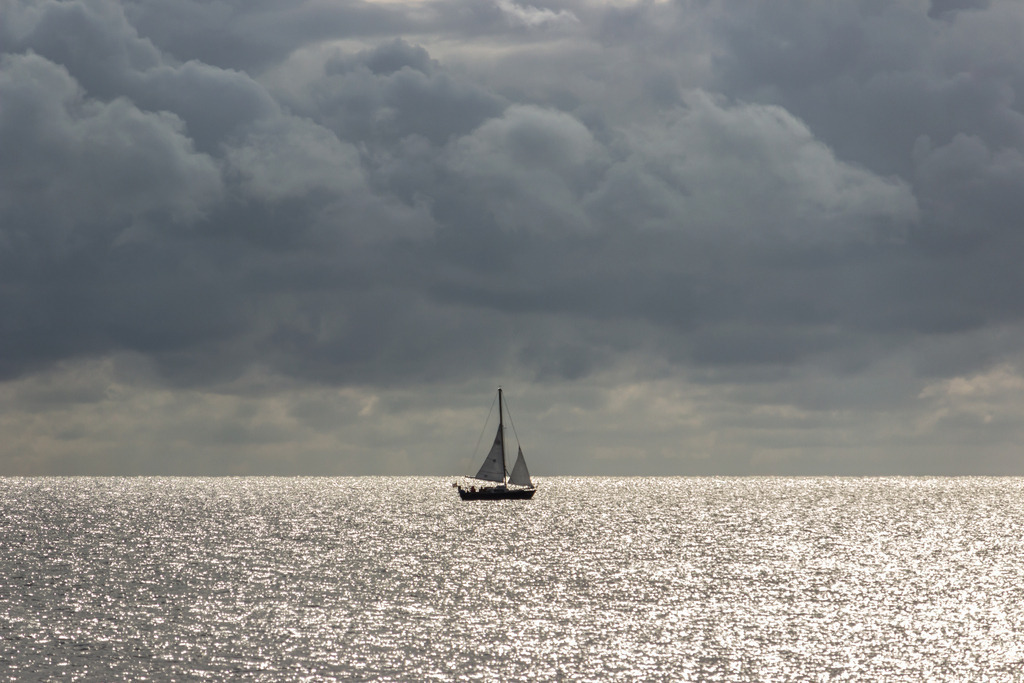Wandbild: Segelboot vor dunklen Wolken | Dieses Wandbild im Querformat zeigt ein Segelboot auf der Ostsee bei Sonnenschein und dunklen Wolken.  - Realisiert mit Pictrs.com