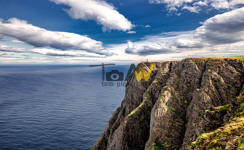 Felsige Steilküste am Nordkapp-Fernblick-Horizont-Norwegen | Das Bild zeigt das Nordkap (norwegisch: Nordkapp), ein bekanntes Schieferplateau in Nordnorwegen. Es liegt auf der Insel Magerøya und ragt etwa 300 Meter steil aus dem Nordpolarmeer (Barentssee) empor. Das Nordkap gilt als der nördlichste über Straßen erreichbare Punkt Europas. Die Landzunge Knivskjellodden auf derselben Insel liegt geografisch noch etwas nördlicher, ist aber nur zu Fuß erreichbar. Der Ort ist eine bedeutende touristische Sehenswürdigkeit, die für ihre atemberaubende Aussicht und die Mitternachtssonne im Sommer bekannt ist. Die Entfernung zum Nordpol beträgt von hier aus nur etwa 2.100 km.  - Realisiert mit Pictrs.com