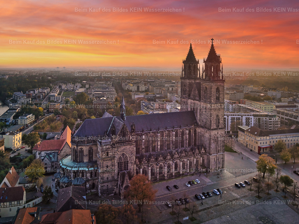 Magdeburg_Luftbild_Dom_Sonnenuntergang_rot_LR_0048 | Dieses Luftbild zeigt den Domplatz im Herzen von Magdeburg aus einer außergewöhnlichen Vogelperspektive. Der Magdeburger Dom erhebt sich mit seinen markanten Türmen über die Platzfläche und bildet den architektonischen Höhepunkt der Aufnahme. Die älteste gotische Kathedrale Deutschlands wirkt wie ein Ankerpunkt am Horizont und verleiht dem Bild eine besondere Tiefe.Die außergewöhnliche Wirkung der Aufnahme entsteht vor allem durch die intensive Bildbearbeitung. Kräftige Rot-, Orange- und Goldtöne dominieren den Himmel und tauchen die gesamte Szene in ein spektakuläres Licht. Mächtige Wolkenformationen verstärken den Eindruck zusätzlich und verleihen dem Motiv eine beinahe surrealistische Atmosphäre. Die Grenzen zwischen Realität und künstlerischer Interpretation scheinen dabei zu verschwimmen.Dieses Luftbild verbindet die historische Architektur des Domplatzes mit einer außergewöhnlichen Licht- und Farbgestaltung und zeigt Magdeburg aus einer Perspektive, die zugleich dokumentarisch und künstlerisch wirkt. - Realisiert mit Pictrs.com
