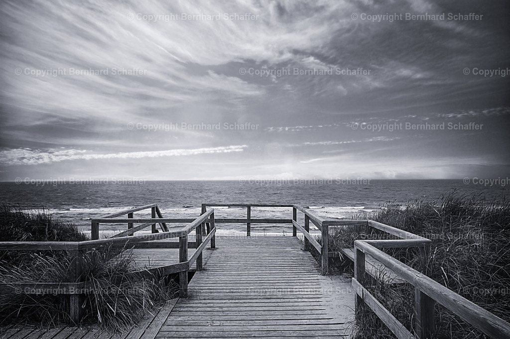 Sylt - Strandtreppe | Eine Plattform aus Holz in Sylt mit einer Treppe zum Strand der Nordsee – schwarz-weiss. - Realisiert mit Pictrs.com