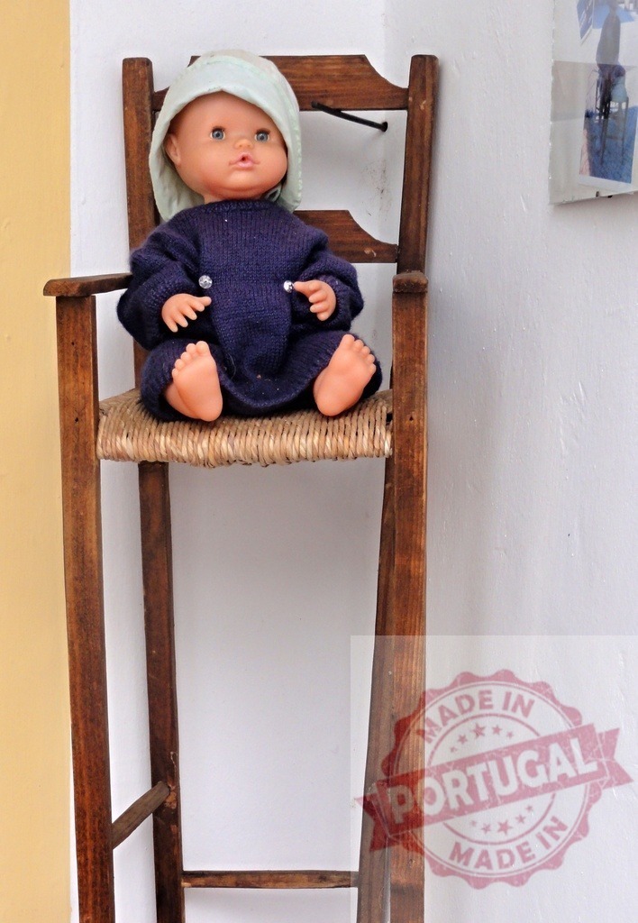 Baby doll wearing blue sweater sitting vintage high chair | Baby doll with a blue sweater and light blue hat sitting on a vintage wooden high chair - Realized with Pictrs.com