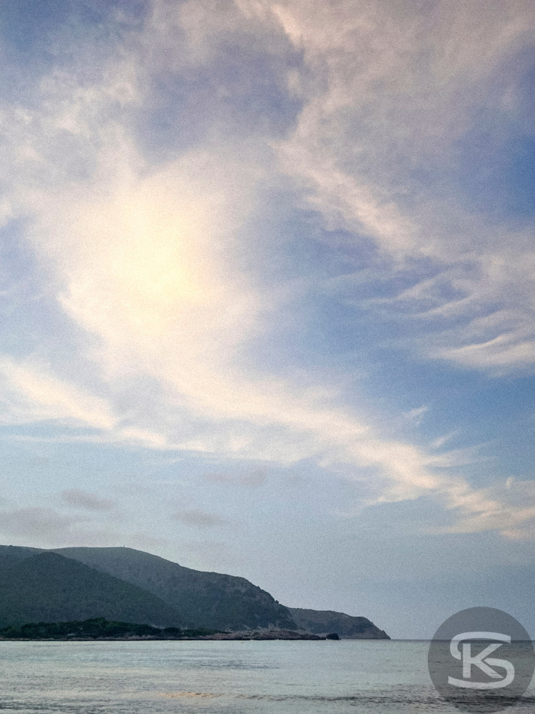 Blaue Stunde an der Cala Agulla – Stimmungsvolles Wandbild aus Mallorca | Abendlicher Ausblick auf das ruhige Meer und die Silhouette der Berge an der Cala Agulla auf Mallorca unter einem weiten, leicht bewölkten Himmel in der Dämmerung. - Realisiert mit Pictrs.com
