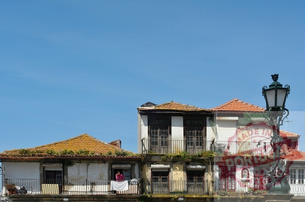Woman on balcony hanging laundry in Porto. Porto - Portugal | Woman hanging clothes on a balcony of old Portuguese houses with a lamp post under a blue sky - Realized with Pictrs.com