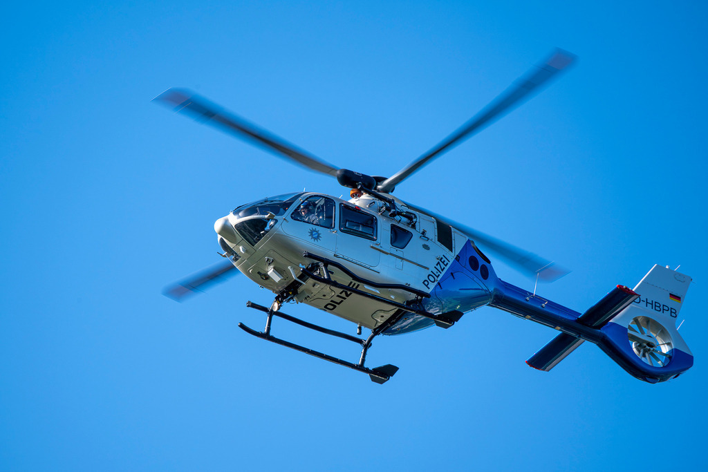 Polizei im Anflug | Ein Polizeihubschrauber der Marke Airbus Helicopters (Kennung D-HBPB) schneidet mit rotierenden Blättern durch das tiefe Blau eines wolkenlosen Himmels. Die dynamische Perspektive von unten fängt die technische Präzision und die Einsatzbereitschaft der Flugmaschine in einem Moment voller Energie ein. - Realisiert mit Pictrs.com