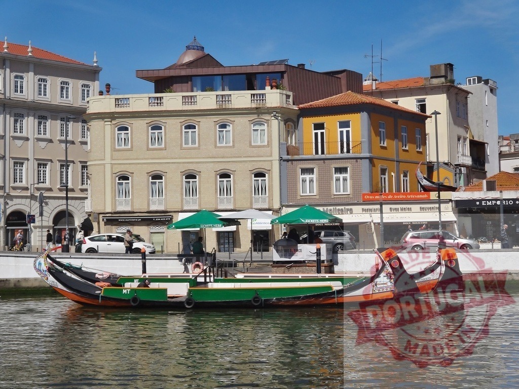 Moliceiro boat cruising canal in Aveiro, Portugal. Aveiro - Portugal | Colorful Moliceiro boat sailing on a canal with traditional buildings along the waterfront - Realized with Pictrs.com