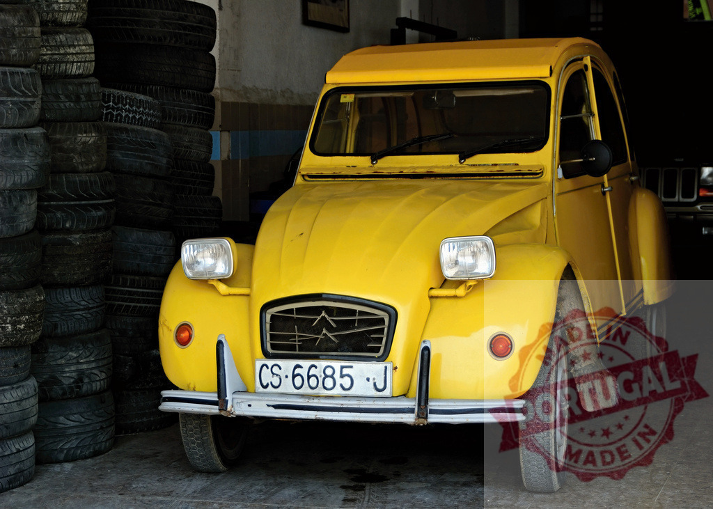 Yellow Citroën 2CV parked in garage next to stack of tires | Classic yellow Citroën 2CV car parked inside a garage next to a stack of tires - Realisiert mit Pictrs.com
