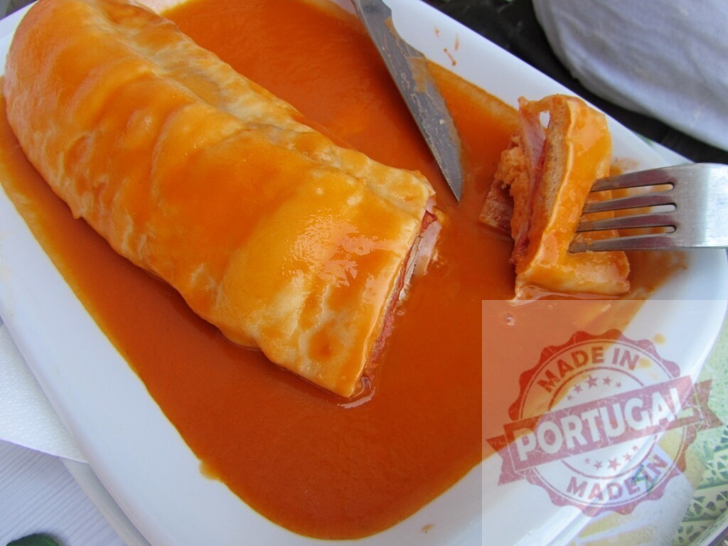 Francesinha sandwich with orange sauce being eaten in Porto Portugal | Francesinha is a traditional Portuguese sandwich swimming in rich orange sauce - Realized with Pictrs.com