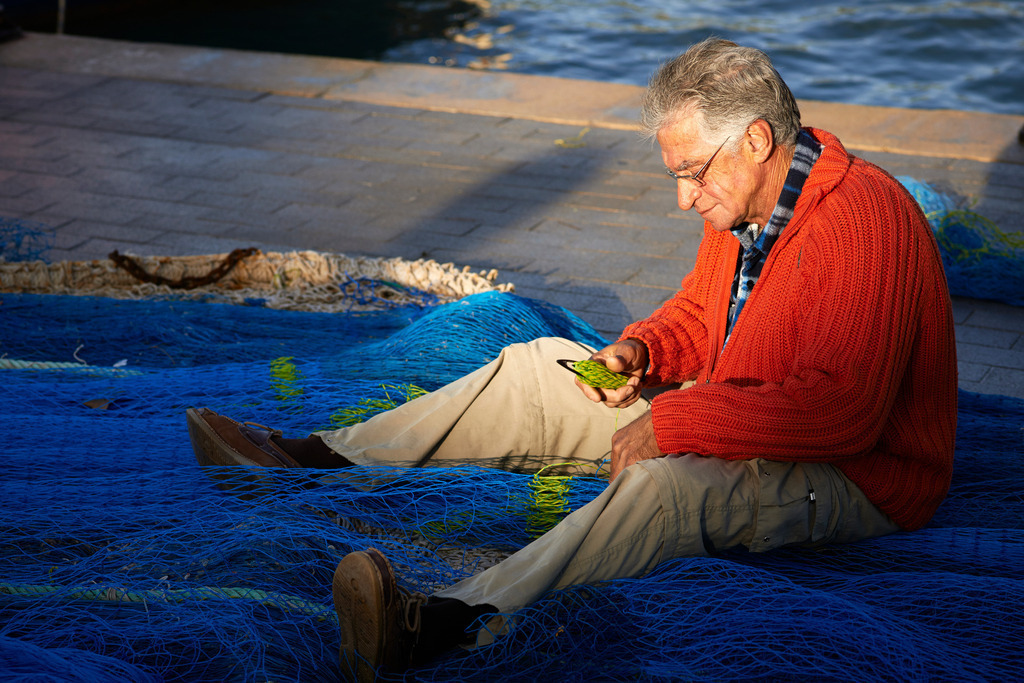 Sitzender Fischer mit rotem Pullover repariert sein Netz | Port d'Andratx, Spanien - December 28, 2013: Fischer mit rotem Pullover am Boden sitzend repariert sein Netz. - Realisiert mit Pictrs.com