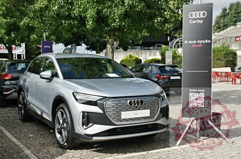 Audi Q4 e-tron electric SUV on display at Carby event | Audi Q4 e-tron parked outdoors at a dealership exhibition with a promotional banner - Realized with Pictrs.com