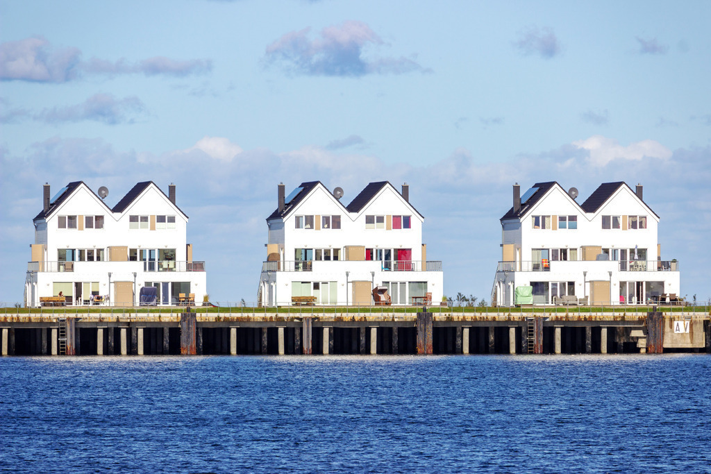 Wandbild: Ferienwohnungen in Olpenitz | Dieses Wandbild zeigt Ferienwohnungen direkt am Meer in Olpenitz. Im Vordergrund ist das Meer zu sehen. In der Mitte befinden sich drei Ferienhäuser und im Hintergrund ist der blaue Himmel mit schönen Wolken zu sehen.  - Realisiert mit Pictrs.com