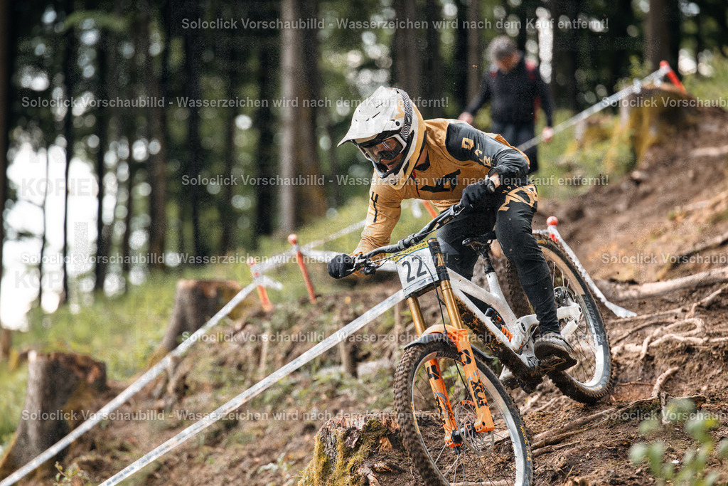 Mountainbiker im Full Speed | Das Foto zeigt einen Mountainbiker in voller Montur, der einen steilen, bewaldeten Hang hinunterfährt. Er ist in Aktion und bereitet sich auf einen Sprung vor. Die Umgebung ist von dichtem Grün und Bäumen umgeben. - Realisiert mit Pictrs.com
