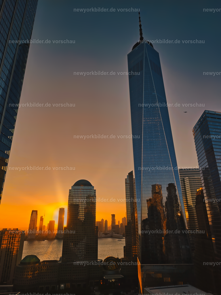 Goldene Stunde am Ground Zero | Die goldene Stunde am Ground Zero ist ein Erlebnis, das man nicht vergisst – und vom M Social Hotel in Downtown wird dieser Moment zu einem echten Highlight. Nach einem ereignisreichen Tag eröffnet sich hier ein Ausblick, der die Seele von New York einfängt: Das One World Trade Center ragt in den Himmel, das futuristische Oculus glänzt im warmen Licht, und die Gedenkbecken der ehemaligen Twin Towers spiegeln die letzten Sonnenstrahlen. Am Horizont verschwindet die Sonne langsam hinter dem Hudson River, während ein Flugzeug aus Newark seine Bahn zieht – ein Detail, das die Dynamik der Stadt unterstreicht. Dieses Foto zeigt die perfekte Symbiose aus Architektur, Geschichte und Natur, eingefangen in einer Stimmung, die Ruhe und Größe zugleich vermittelt. Ein Moment, der beweist, wie einzigartig Downtown Manhattan bei Sonnenuntergang ist.