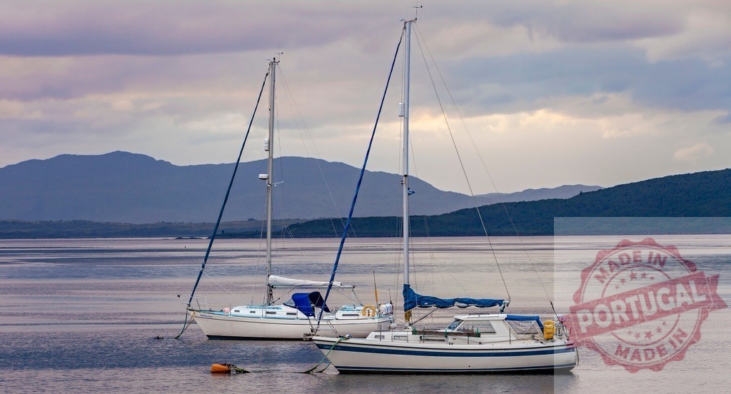 Sailboats moored on calm lake waters under cloudy sky | Two sailboats are moored on tranquil lake waters with mountains and a cloudy sky - Realisiert mit Pictrs.com