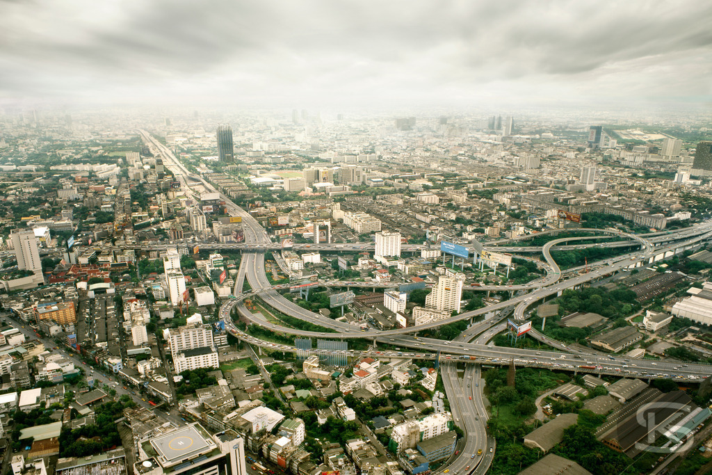 Luftbild von Bangkok (2006) mit massivem Autobahnkreuz, aufgenommen vom Baiyoke Tower | Eine weitläufige Luftaufnahme von der Aussichtsplattform des Baiyoke Sky Tower in Bangkok (Thailand) aus dem Jahr 2006, die das geschäftige Stadtbild und einen komplexen, vielspurigen Autobahnknotenpunkt bei Tag zeigt. Die Aufnahme fängt die dichte urbane Entwicklung und das weitläufige Verkehrsnetz der Metropole ein. - Realisiert mit Pictrs.com