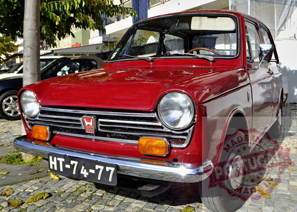 Gleaming Red Honda N600 parked on cobblestone street | Classic red Honda N600 parked on a cobblestone street, showcasing its vintage charm and excellent condition - Realized with Pictrs.com