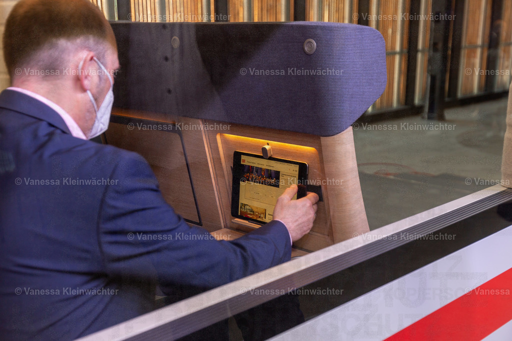 Deutsche Bahn stellt neues ICE-Design vor | Blick durchs Fenster des ICE-Modells. Zu sehen ist eine Person mit FFP2-Maske und der Hand am Tablet, das sie in die Halterung am Sitz gestellt hat.

Berlin, 18.05.2022: In der STATION stellt die Deutsche Bahn ihr neues ICE-Design mit einem begehbaren Modell vor. Neuerungen sind etwa das Material der Sitze und die Ergänzung einer Tablethalterung. Ende 2023 sollen die ersten ICEs mit dem neuen Design auf die Schiene kommen. - Realisiert mit Pictrs.com