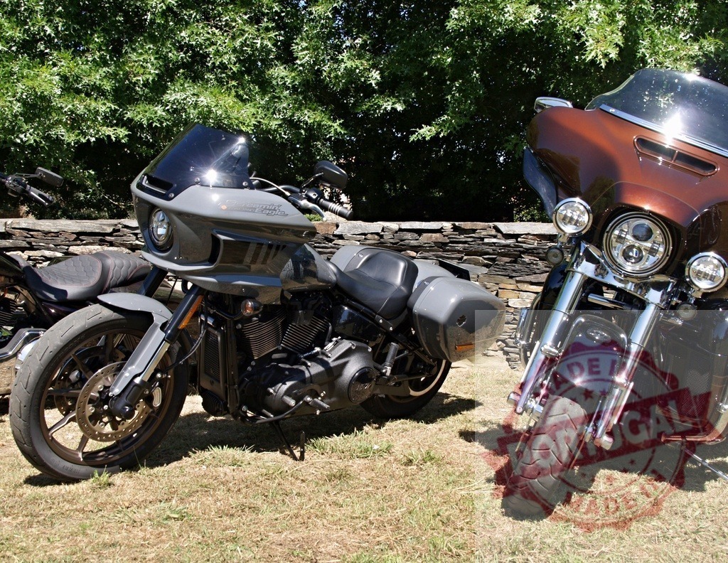 Two Harley-Davidson motorcycles parked on grass near a stone wall | Two Harley-Davidson motorcycles parked on a grassy area, showcasing their designs and features - Realisiert mit Pictrs.com