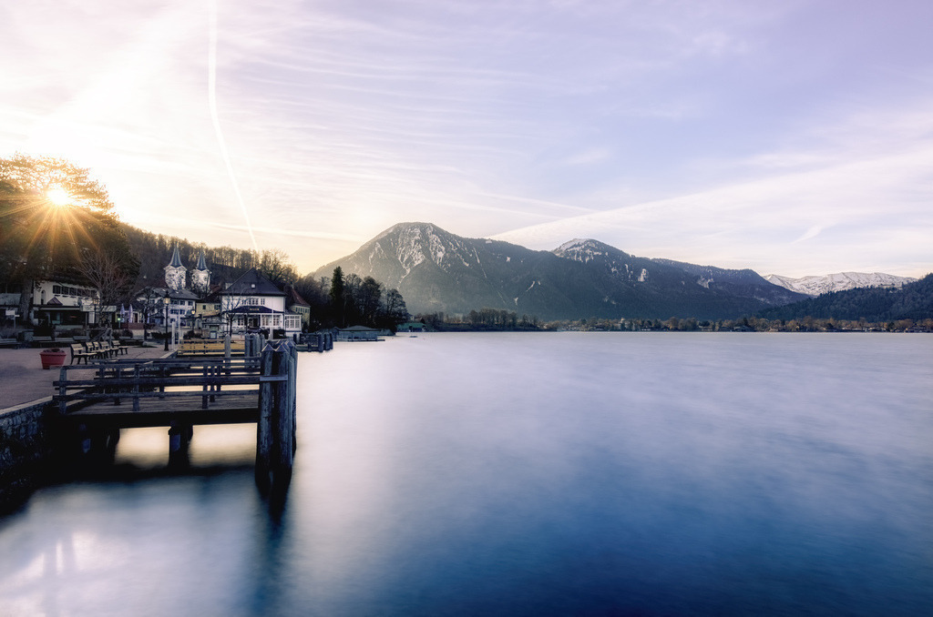 Sonnenaufgang im Ort Tegernsee | Das Bild zeigt den Tegernsee in Bayern, Deutschland, eine beliebte Erholungsregion südlich von München. Der See liegt in den Bayerischen Alpen auf 726 Metern über dem Meeresspiegel. An seinen Ufern liegen Gemeinden wie Rottach-Egern, Bad Wiessee und die Stadt Tegernsee. Die Region ist bekannt für ihre typisch bayerische Lebensart, Naturidylle und Freizeitmöglichkeiten wie Wandern und Segeln. Das spezifische Motiv des Sonnenaufgangs wird unter anderem für hochwertige Wandkalender verwendet.  - Realisiert mit Pictrs.com