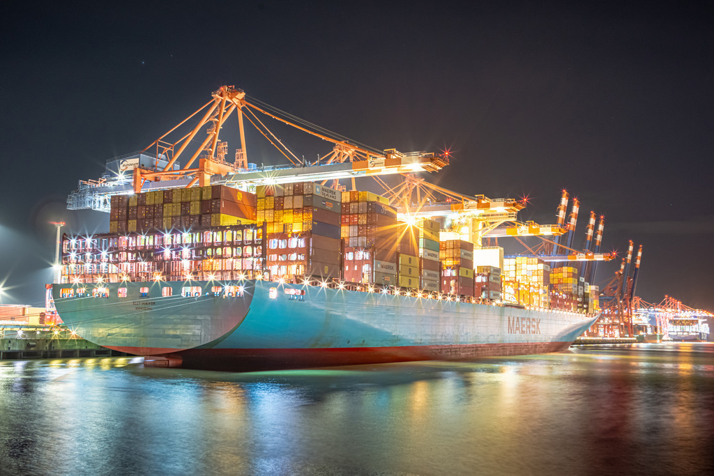 Nachts am Burchardkai Nr.3 | Das Bild zeigt eine nächtliche Szenerie im Hamburger Hafen am Burchardkai, wo mehrere riesige Containerschiffe angedockt sind. Die Schiffe erheben sich majestätisch in die Dunkelheit und werden von einer Flut von Lichtern beleuchtet, die vom Hafen und von den Schiffen selbst ausgehen. Das Bild fängt die Hektik und den Puls des Hafens in der Nacht ein und vermittelt einen Eindruck von der enormen Größe und dem Einfluss dieses wichtigen Handelszentrums.